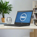 A certified refurbished Dell Latitude E7470 i5-6300U 8GB RAM 128GB SSD 14 FHD W10P laptop, displaying the Dell logo, sits on a white desk beside a silver mug and spoon, with a green plant and bookshelf blurred in the background.