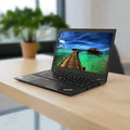 A refurbished Lenovo ThinkPad T460s Laptop 14" i7-6600U 8GB 256GB SSD Touch Win 10 Pro sits on a light wooden desk, its screen showing a tropical beach. A green potted plant and large windows are blurred in the background.