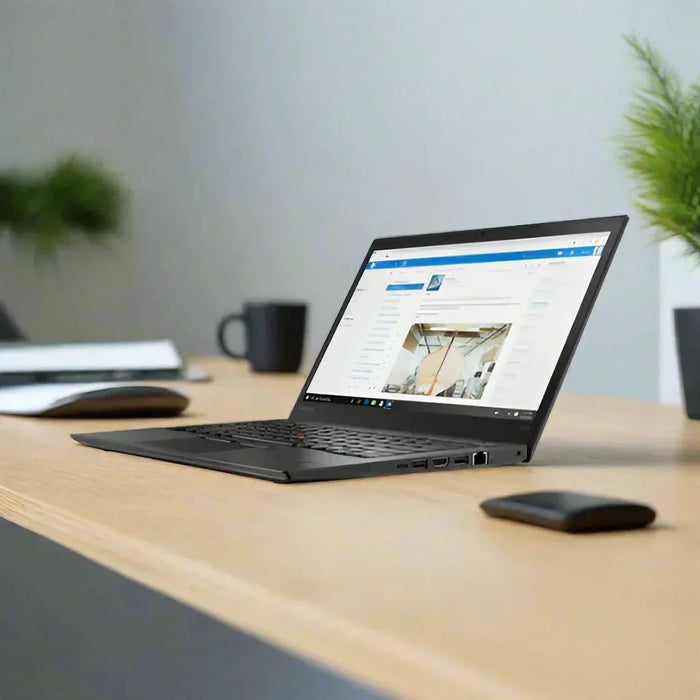 A Lenovo ThinkPad T470s i5 7200U 2.5GHz 8GB 256GB SSD sits open on a wooden desk displaying a webpage, with a wireless mouse, black mug, closed notebook, and two green potted plants in a modern office setting.